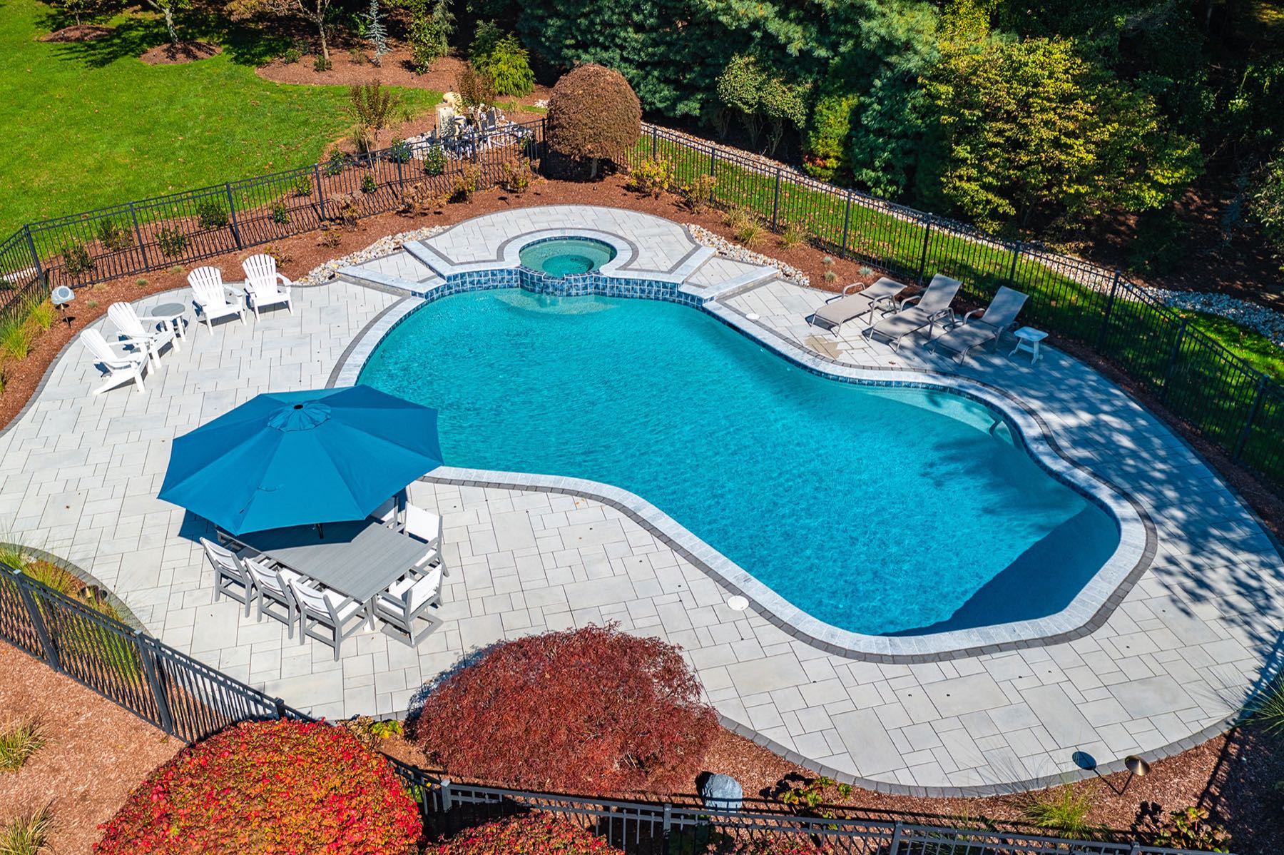 Aerial view of a renovated free-form pool with a spa, paver deck and fenced yard in New Jersey