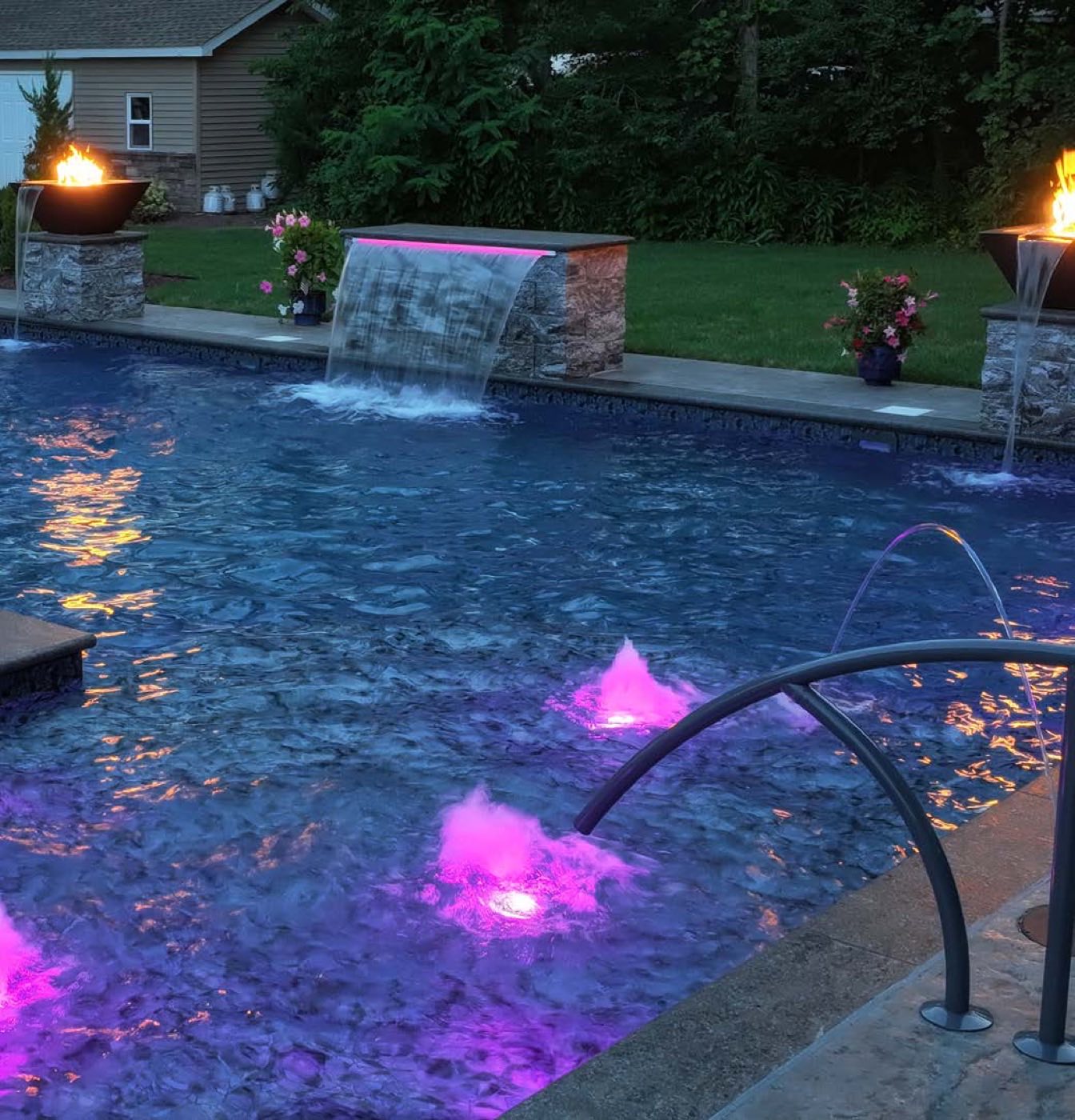 Pool at night with color LED lights, sheer descent and fire bowls