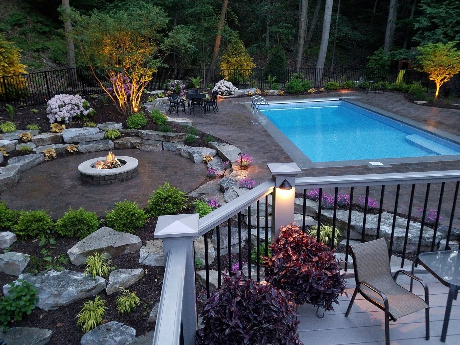 Renovated pool and backyard at dusk with fire pit, stone and landscape lighting